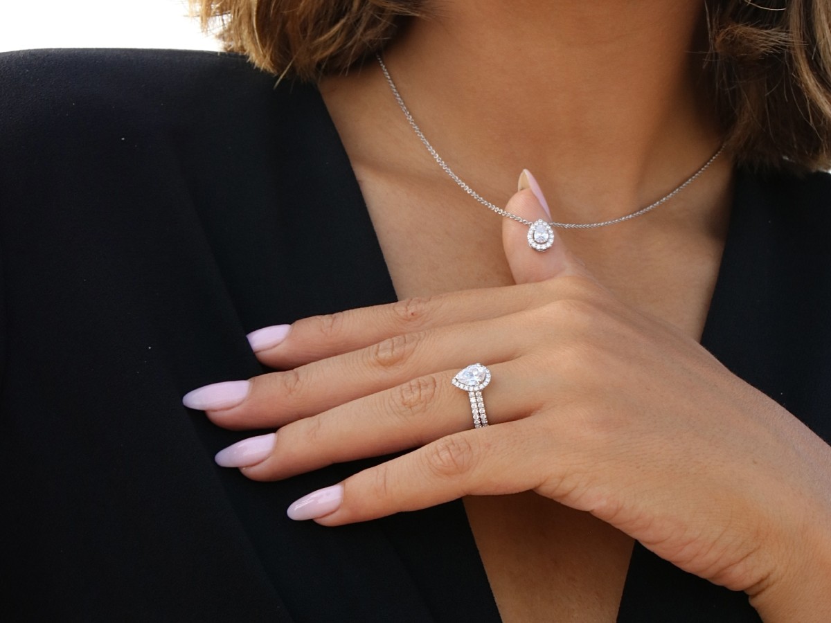 Main de femme portant une bague de fiançailles en diamant de laboratoire et un collier assorti, sur fond noir – bijou raffiné signé Laveran Paris